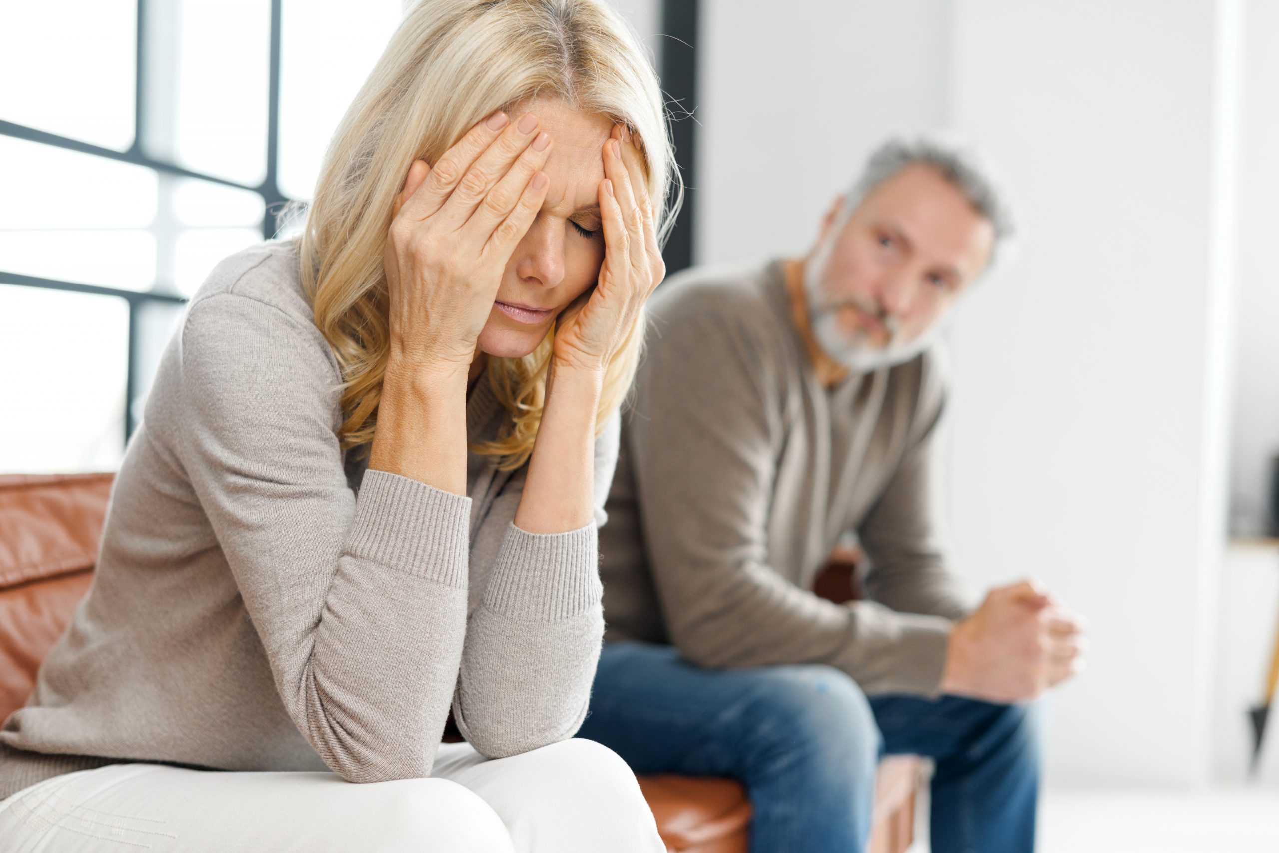 Mature couple relation problem. Upset woman feeling sad and crying after have an argument at home, sad or depressed woman sitting on sofa with her husband, man in defocus sits near